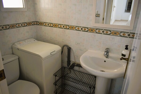 Uma casa de banho pequena com sanita, máquina de lavar, lavatório e paredes revestidas a azulejos.