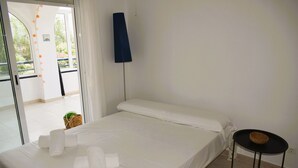 A clean, well-lit room with a bed, a small table with a basket, and a view of the outdoors through a glass door. - Anacasa Royal Playa les Marines AP1213 (Denia)