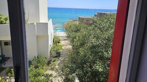 A view of a coastal area with a clear sky, a sandy path leading to the beach, and a building with a white facade.
