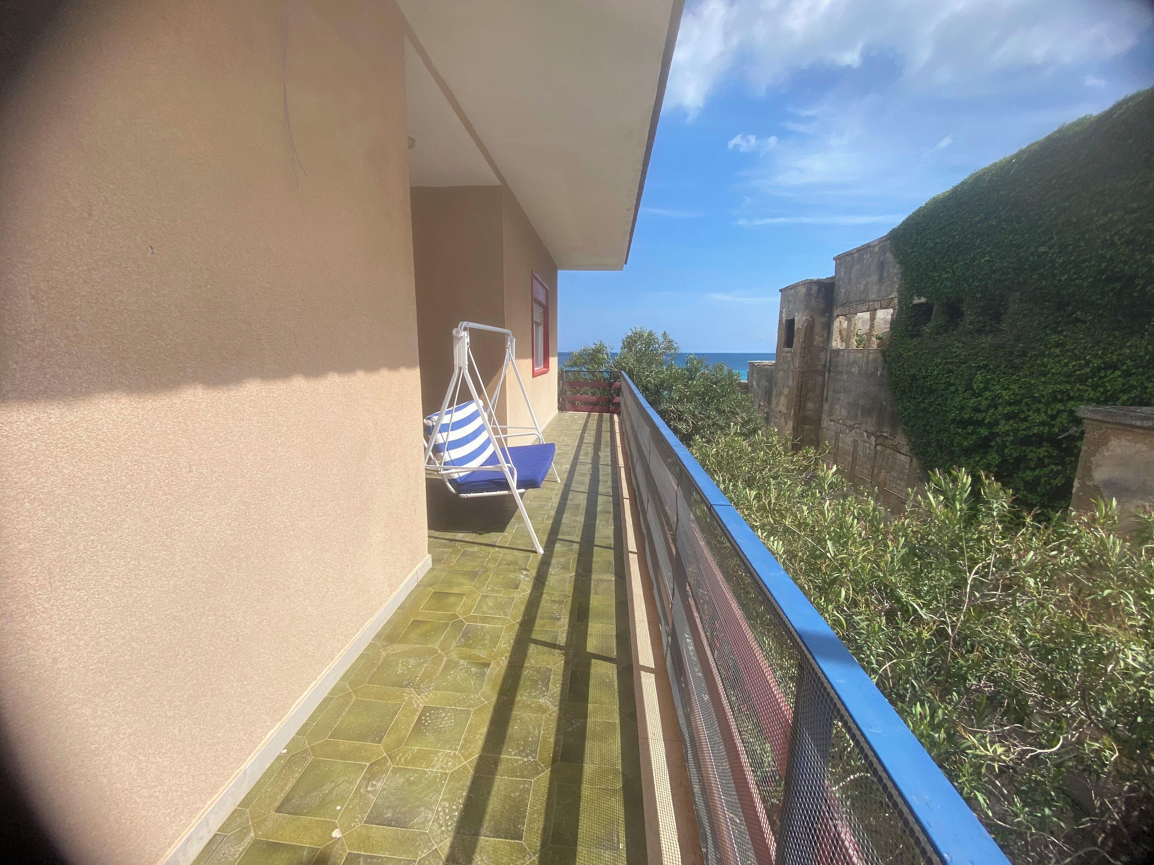 A balcony with a swing chair, a view of the sea, and a stone wall.