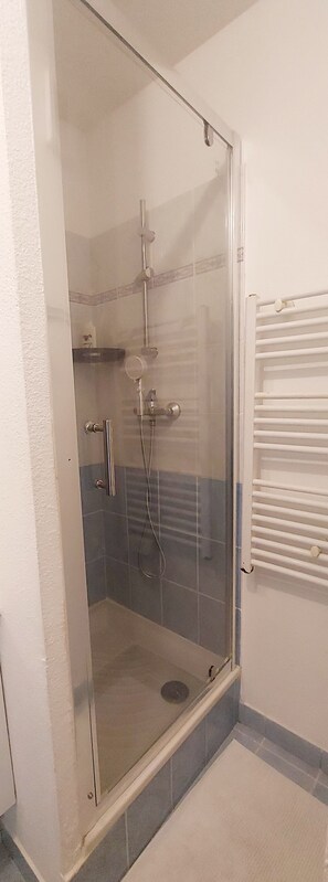 A glass-enclosed shower with a handheld showerhead, a wall-mounted faucet, and a drain. - Cosy 2-room apartment - Centre Villefranche-sur-Saône with garage (Villefranche-sur-Saône)