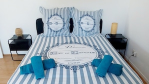 Ein Bett mit einer blau-weiß gestreiften Bettdecke und passenden Kissen, zwei blaue Handtücher und ein dekoratives Kopfkissen mit Text.