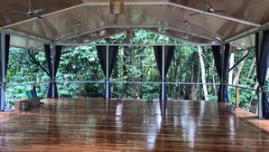 A spacious indoor area with a wooden floor, large windows, and ceiling fans.
