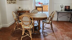 A dining area with a wooden table and four wicker chairs, a kitchen visible through an open doorway, and a ceiling light fixture.