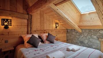 A cozy wooden room with a bed, two wall sconces, and a stone wall.
