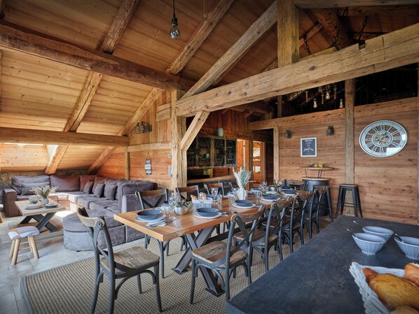 Ein rustikaler Essbereich aus Holz mit einem langen Tisch, der für eine Mahlzeit gedeckt ist, umgeben von Stühlen.