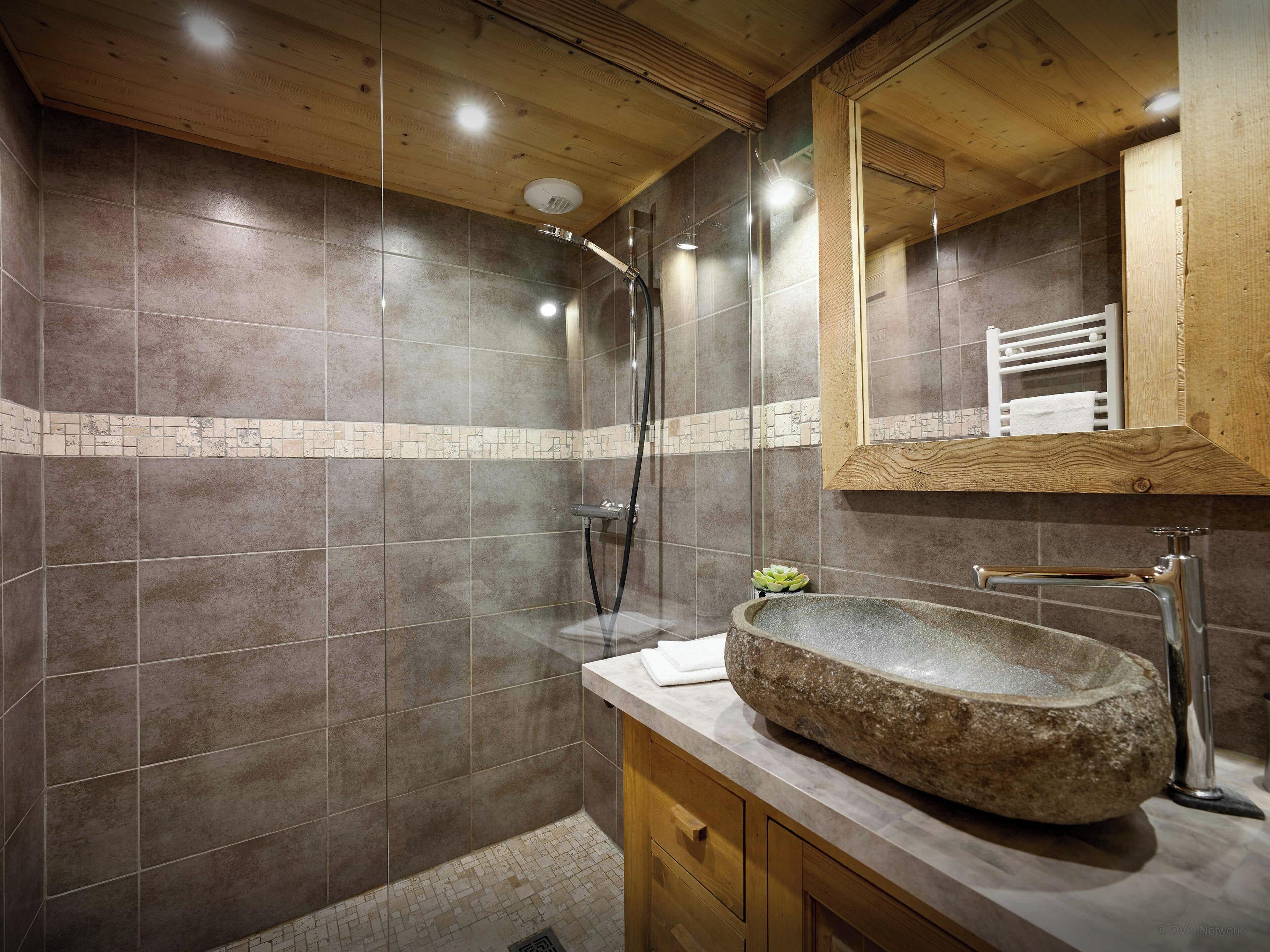 Une salle de bain moderne avec un lavabo en pierre, un meuble-lavabo en bois et un grand miroir.