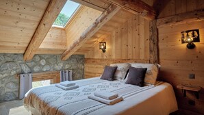 Un dormitorio de cabaña de madera con techo inclinado, pared de piedra y cama con ropa de cama estampada.