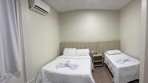 A hotel room with two beds, a nightstand, and an air conditioning unit.