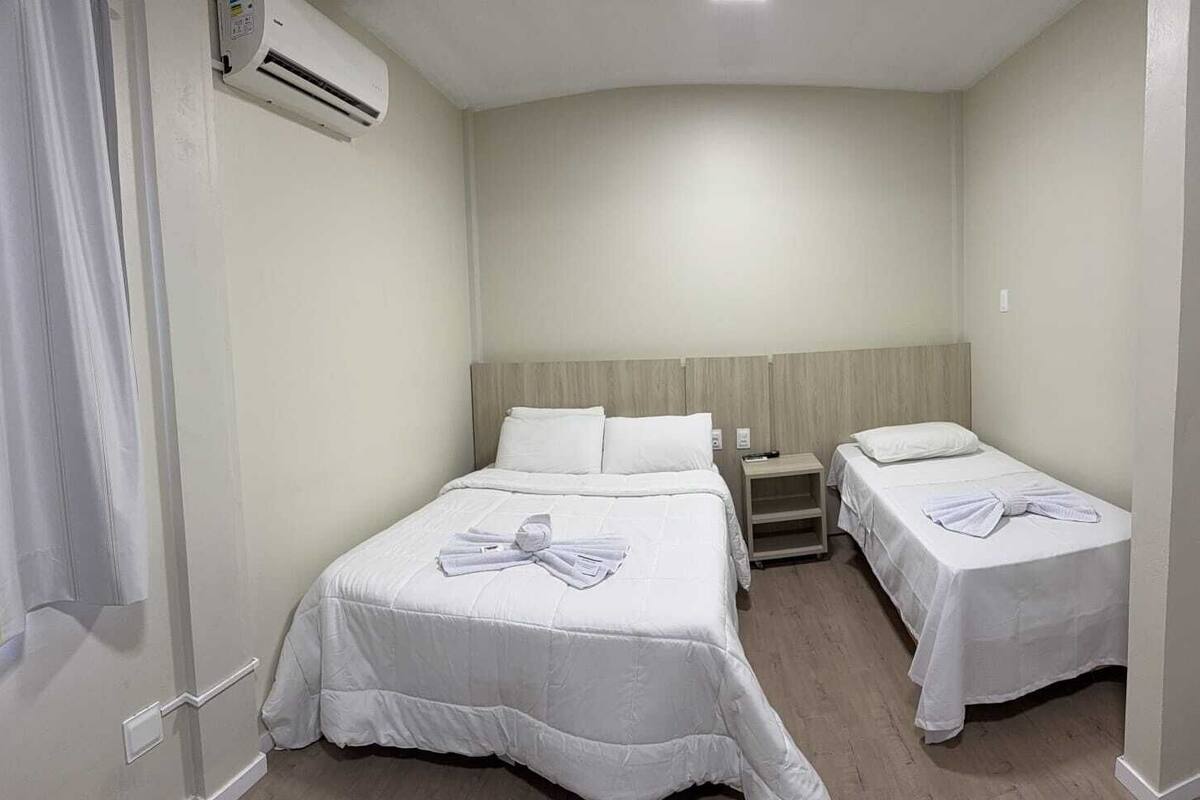 A hotel room with two beds, a nightstand, and an air conditioning unit.