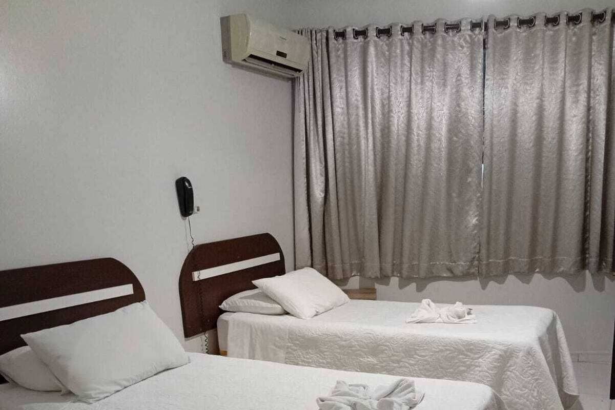 A hotel room with two beds, a telephone, an air conditioner, and a curtain.
