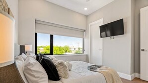 Un dormitorio moderno con un ventanal grande, un televisor de pantalla plana y una cama con ropa blanca.