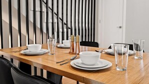 Una mesa de comedor dispuesta con platos blancos, cuencos y vasos transparentes, con una escalera moderna al fondo.