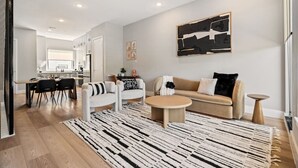 Una sala moderna con un sofá, un sillón y una mesita de centro, un comedor con sillas y una cocina al fondo.