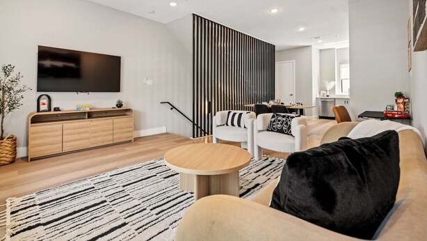 Una sala moderna con un televisor de pantalla plana, un mueble de madera, una mesa de centro redonda y un sofá con cojín negro.