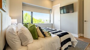 A bedroom with a bed, a window, a flat-screen TV, and a door. - DT Designer Gem |  FirePit, Pool Table, Telescope (Fort Worth)