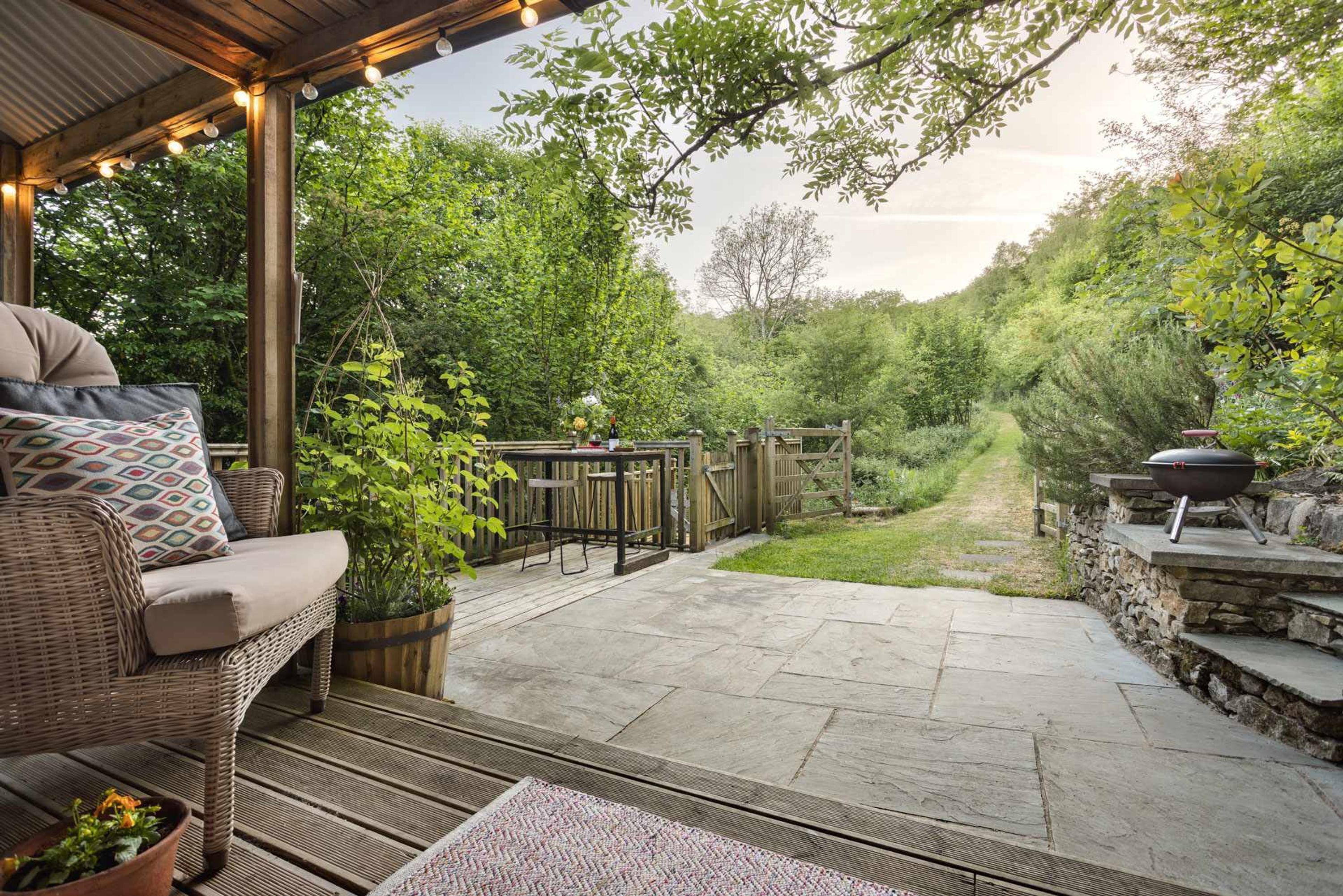 A covered patio with a wicker sofa, a grill, and a stone pathway.