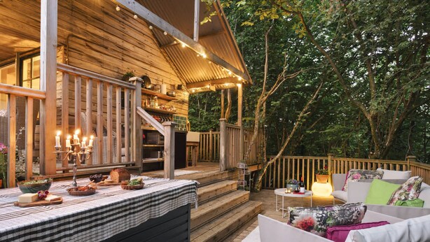 A wooden deck with a dining table set for a meal, surrounded by outdoor furniture. - The Hut Rawsons in Levens (Kendal)