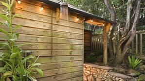 A wooden cabin with a stone wall and wooden deck. There are plants and a bottle of wine on the deck. - The Hut Rawsons in Levens (Kendal)