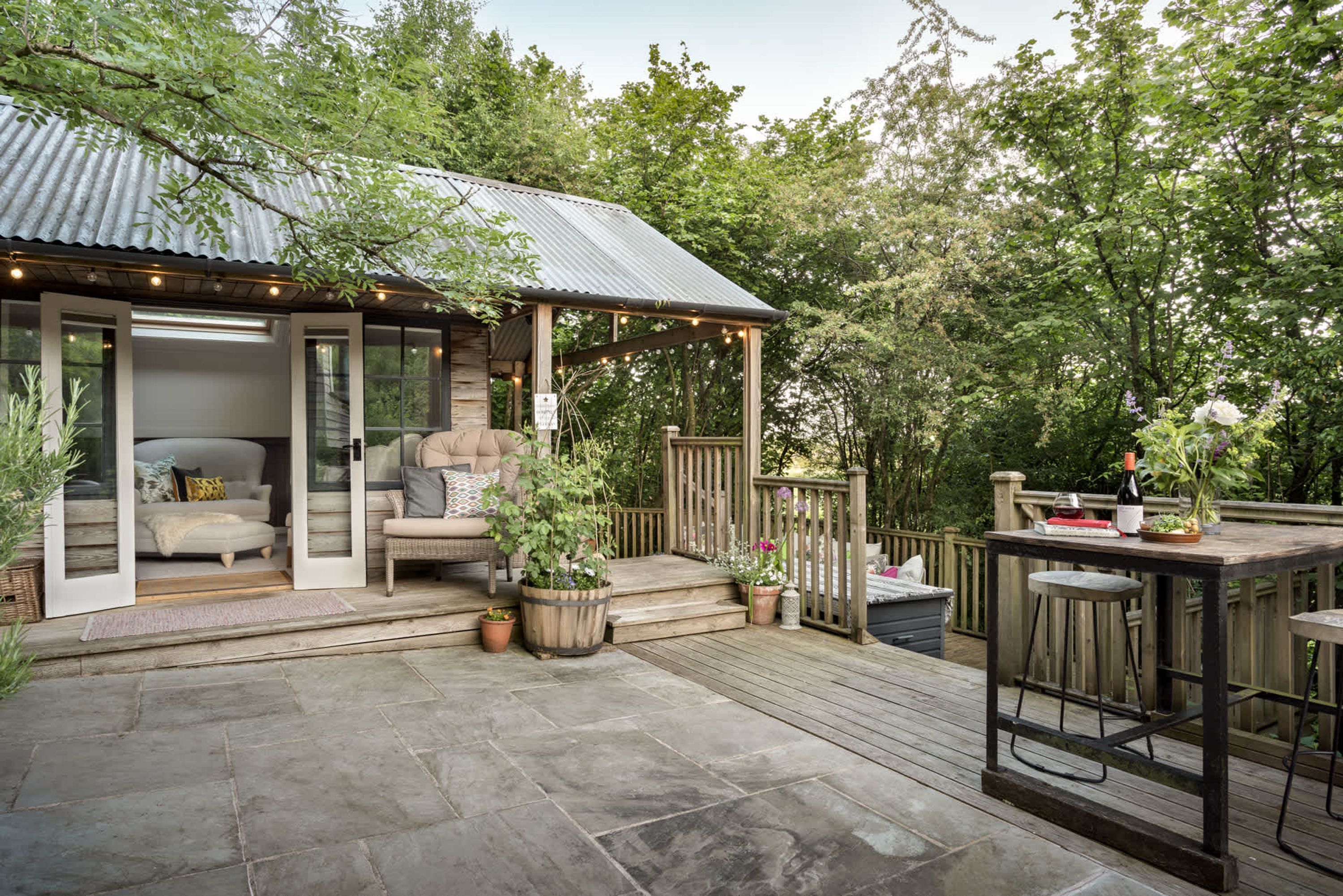 A wooden deck with a covered seating area, stone flooring, and potted plants.