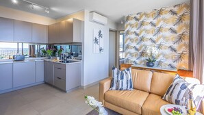Eine moderne Küche mit integrierter Kochinsel, ein Essbereich mit einer Sitzecke und ein Wohnzimmer mit einer Wand in Musteroptik.