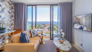 Ein modernes Hotelzimmer mit großem Balkon, einer Couch, einem kleinen runden Tisch und einem Wand-Fernseher.