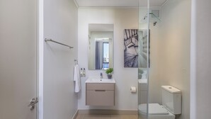 Ein modernes Badezimmer mit Duschkabine aus Glas, Waschbecken mit Spiegel darüber und Toilette.