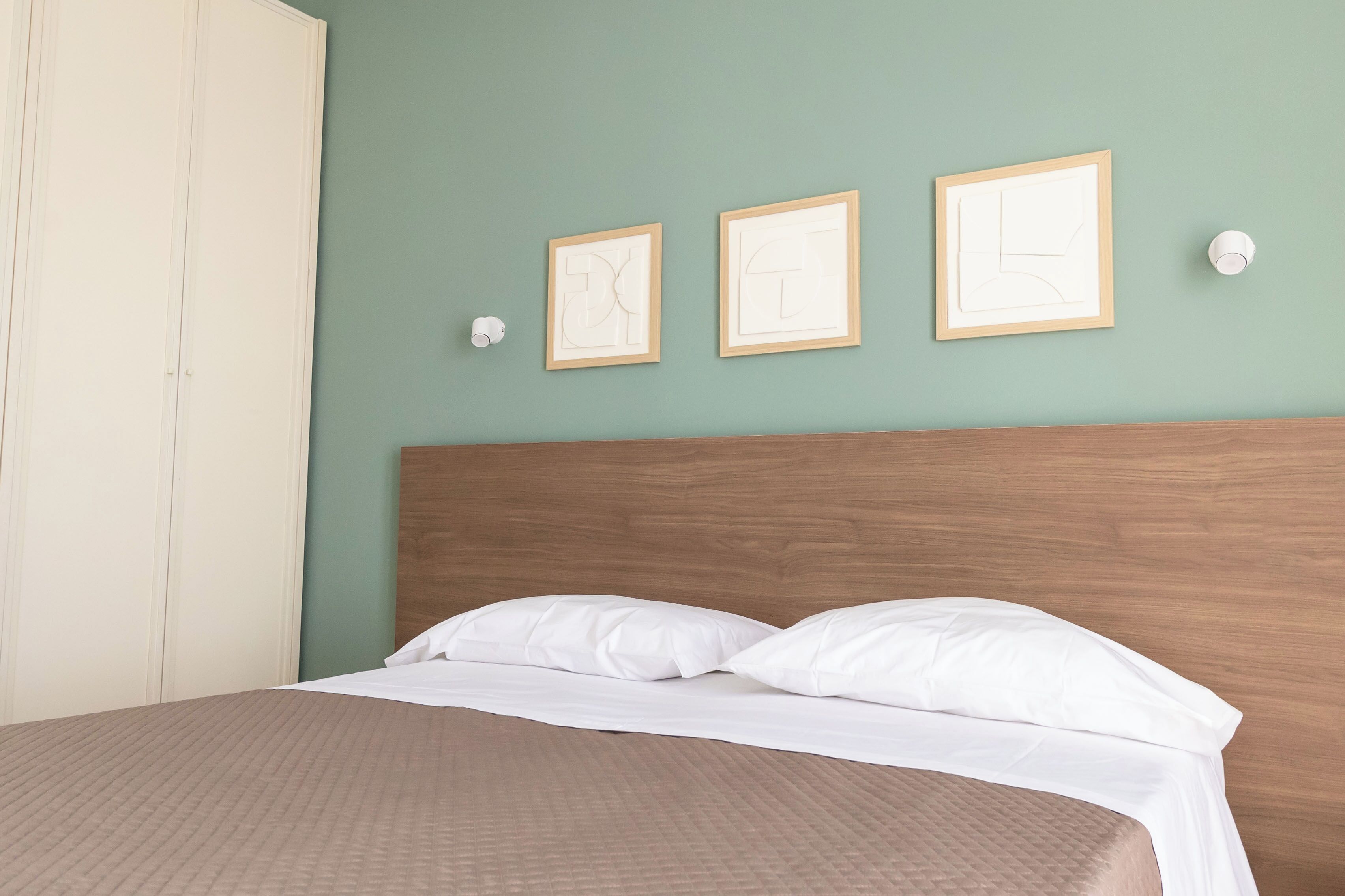 Una cama bien hecha con ropa blanca, un cabecero de madera y tres cuadros en la pared.