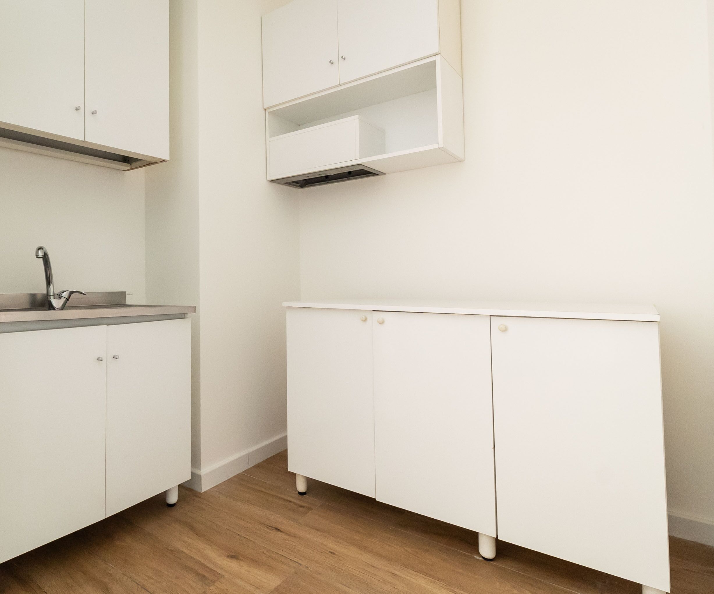 Une cuisine avec des armoires blanches, un évier en acier inoxydable et un plancher en bois.