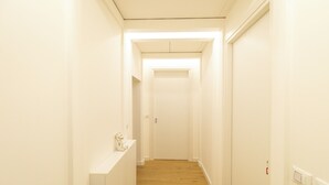 Un couloir étroit, doté d’un plancher en bois et de murs blancs, qui mène à une porte fermée au bout.