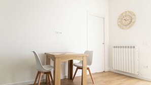 Un coin repas avec une table en bois et deux chaises, une porte blanche et une horloge fixée au mur.