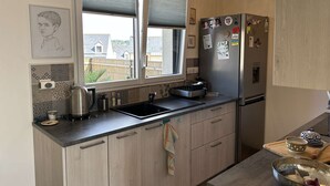 Une cuisine moderne dotée d’une grande fenêtre, d’appareils électroménagers en acier inoxydable et d’un luminaire suspendu.