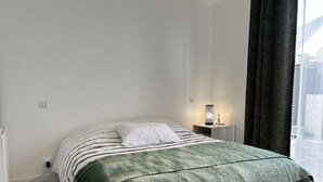 Une chambre à coucher bien rangée, avec un lit, une table de chevet et une petite table de nuit sur laquelle se trouve une lampe.