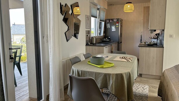 Un espace de vie compact comprenant un coin repas, une cuisine et une porte-fenêtre coulissante donnant sur une terrasse extérieure.
