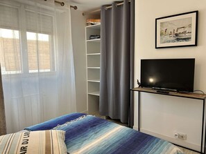 A bedroom with a bed, a TV, a wardrobe, and a window with curtains. - Courtyard house in Erquy | 4 guests | Ref 669 (ERQUY)