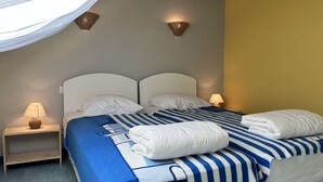Ein Doppelbett mit einer blau-weiß gestreiften Bettdecke, zwei weiße Kissen und zwei weiße Handtüchen, die am Fuß des Bettes gefaltet sind. Zwei Nachttische mit Lampen stehen bereit, und der Raum hat eine gelbe Akzentwand.