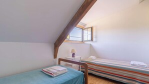 A small, single-room accommodation with a sloped ceiling, a window, a bedside table with a lamp, and a bed with a striped bedspread. - Family house in Pléneuf | 10 guests | Ref 1010 (PLENEUF VAL ANDRE)