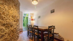 A dining area with a stone wall, wooden table, and chairs. - Family house in Pléneuf | 10 guests | Ref 1010 (PLENEUF VAL ANDRE)