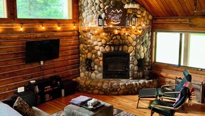A cozy cabin interior with a stone fireplace, wooden walls, a large sofa, and a television.
