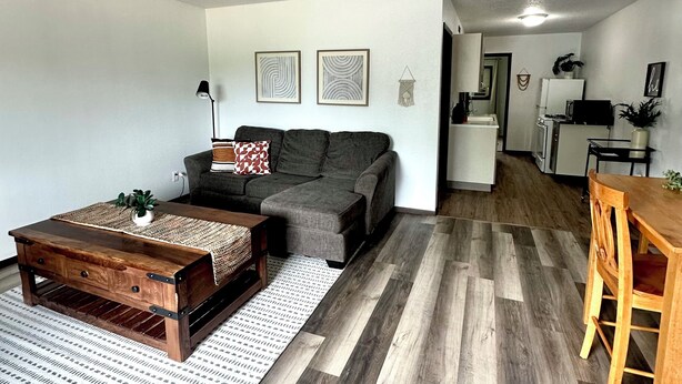 Una sala moderna con un sofá gris, una mesa de centro de madera y una zona de comedor con una mesa y sillas de madera.