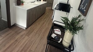 Una cocina moderna con armarios de madera, una isla central y una encimera negra. Hay una pequeña mesa negra con una planta y un cuadro enmarcado.