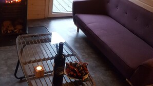 Une pièce chaleureuse avec une cheminée, un canapé et une table sur laquelle se trouvent une bouteille et des en-cas.