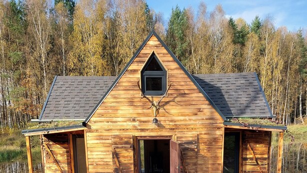 Une cabane en bois avec un quai s’avançant dans un lac paisible, entourée d’arbres.