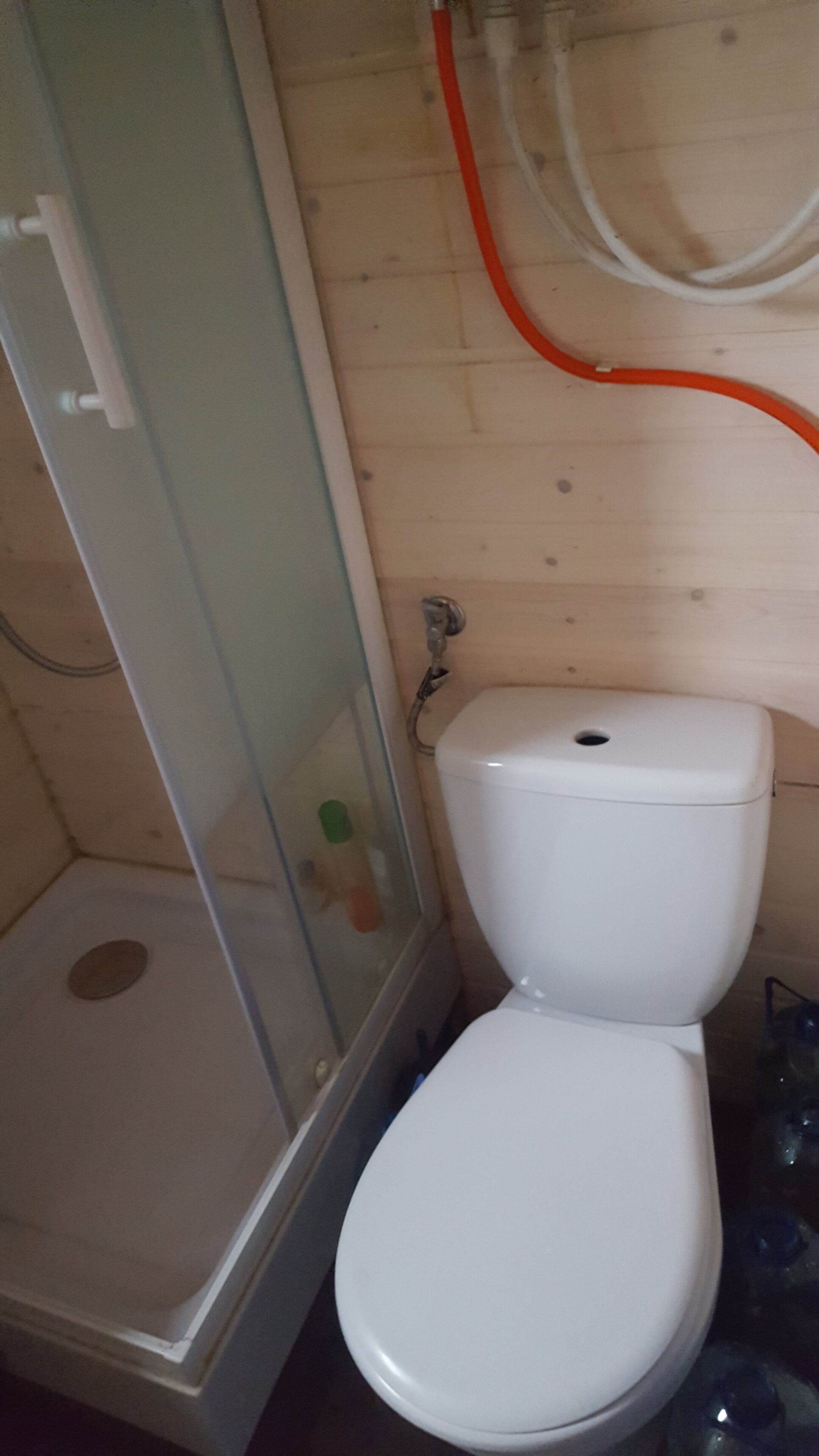 A bathroom with a white toilet, a glass shower enclosure, and visible plumbing pipes.