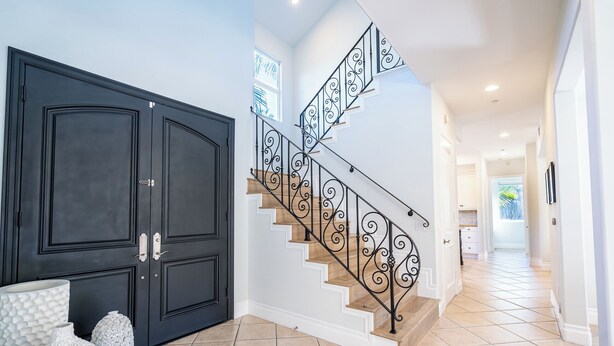 Ein modernes Interieur mit einer dunklen Holztür, einer Treppe mit aufwendigen schwarzen Geländern und einem gefliesten Boden.