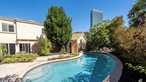Ein Pool mit geschwungener Kante, umgeben von einem angelegten Garten und einem Gebäude mit beiger Fassade.