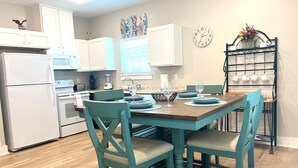 A modern kitchen with white cabinets, a wooden dining table with teal chairs, and a coffee station with cups and a vase of flowers. - New Listing!  Oasis Bungalow (Rockport)