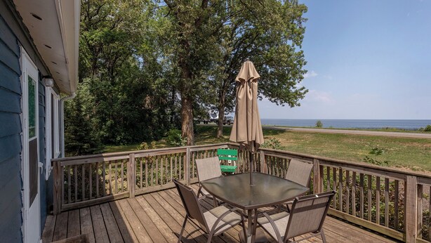A wooden deck with a table and chairs, overlooking a grassy area and the ocean.