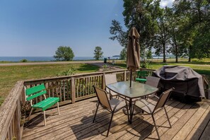 A wooden deck with a glass table and chairs, a green bench, and a barbecue grill.