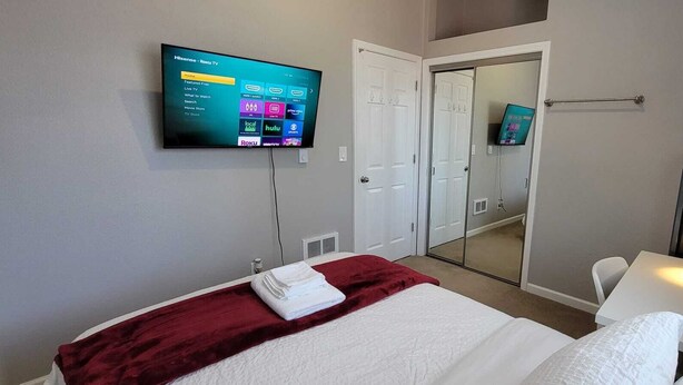 A hotel room with a bed, a TV mounted on the wall displaying a Roku TV interface, a mirror, and a bathroom with a sink and towel rack. - Easy access to I-5, Hwy 99. 1 bus stop from Aurora Transit Center. (Edmonds)